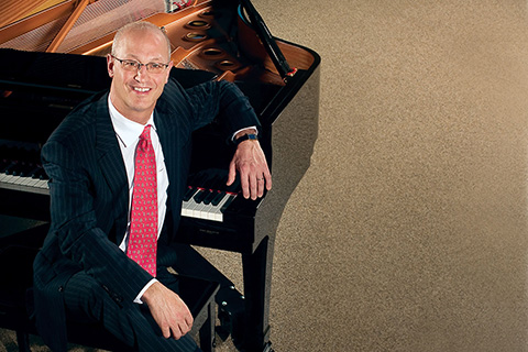 A man in a dark suit sits down at a piano